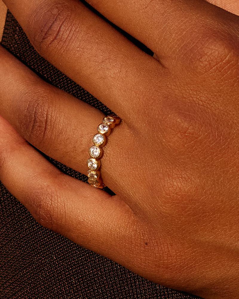 Anello Amélia con una fila di pietre scintillanti incastonate a castone in una fascia dorata testurizzata, indossato al dito.