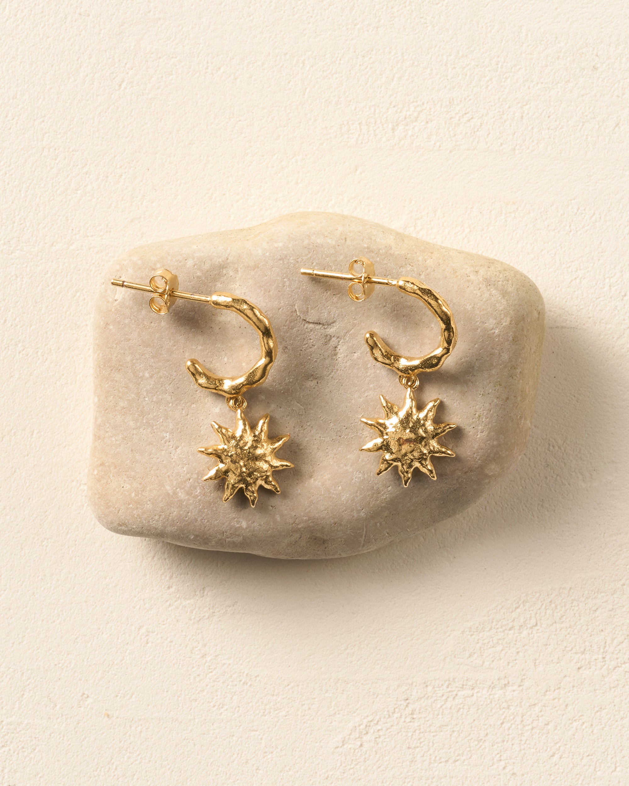 Gold Solé hoop earrings with sculpted, hammered suns on a light stone.