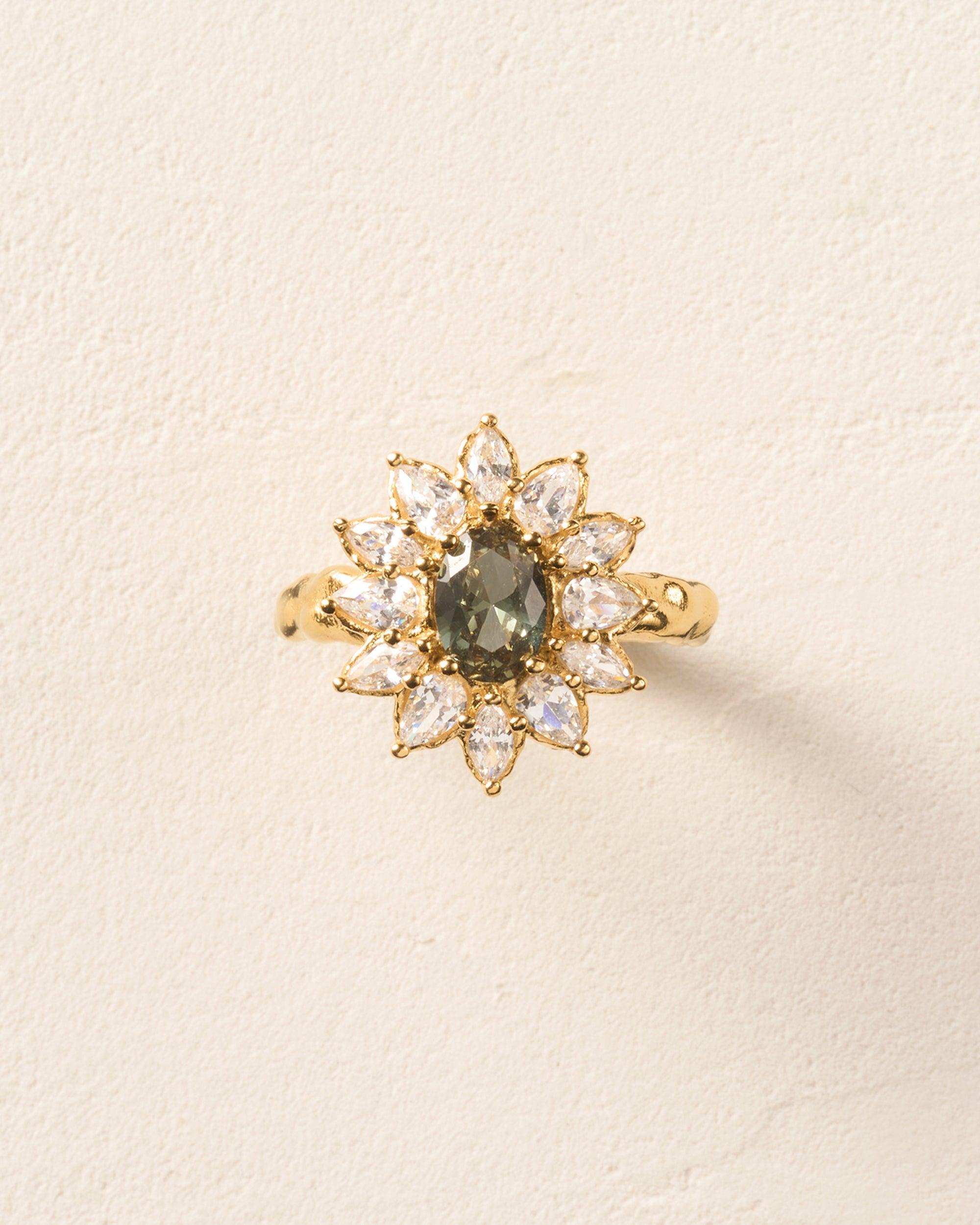 Calia cocktail ring: gold band, central blue-green stone, pear-cut clear stones in flower setting.