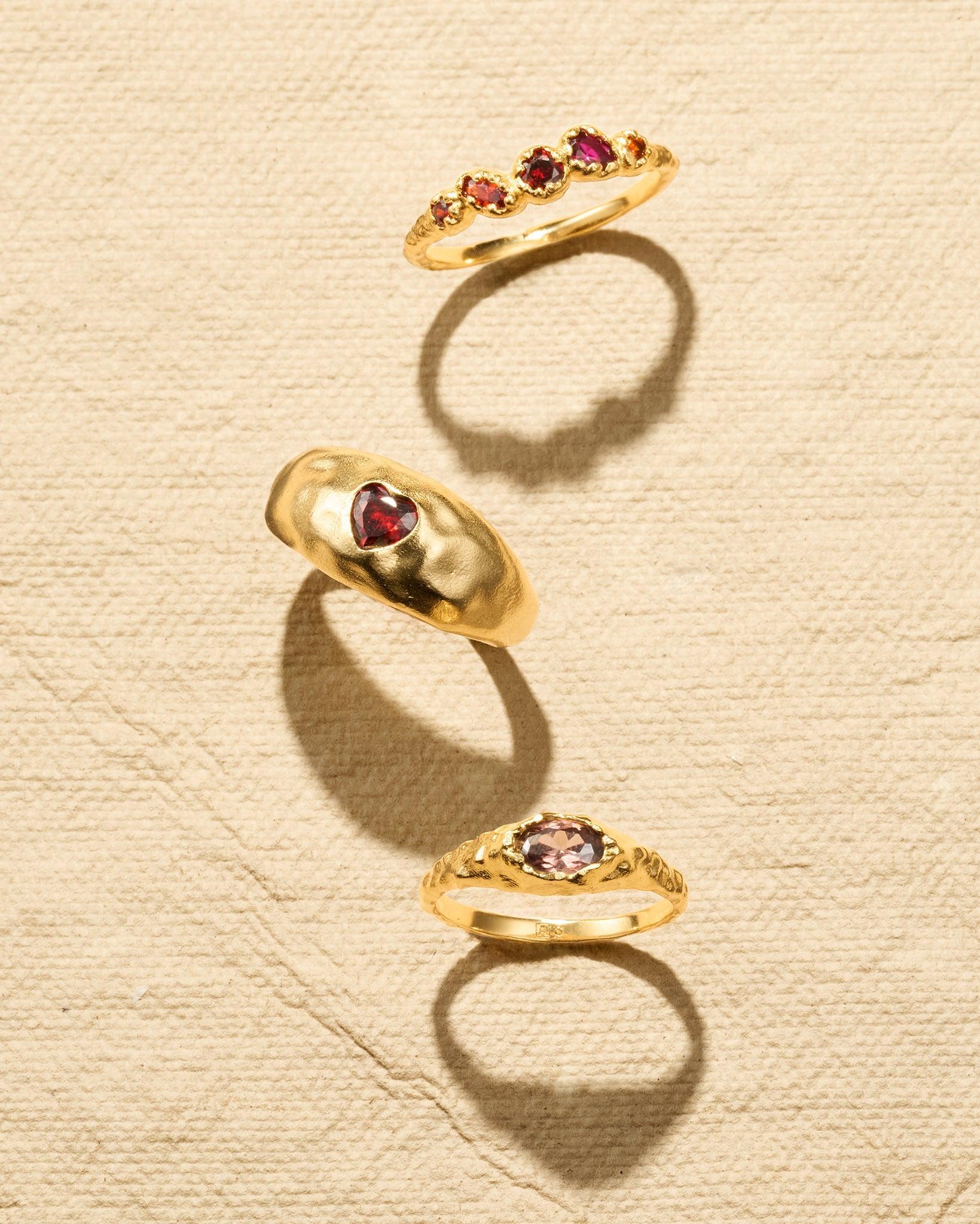 Anillo cúpula Maria Mini fino y dorado con una textura martillada y una piedra marrón facetada, sobre un fondo beige.