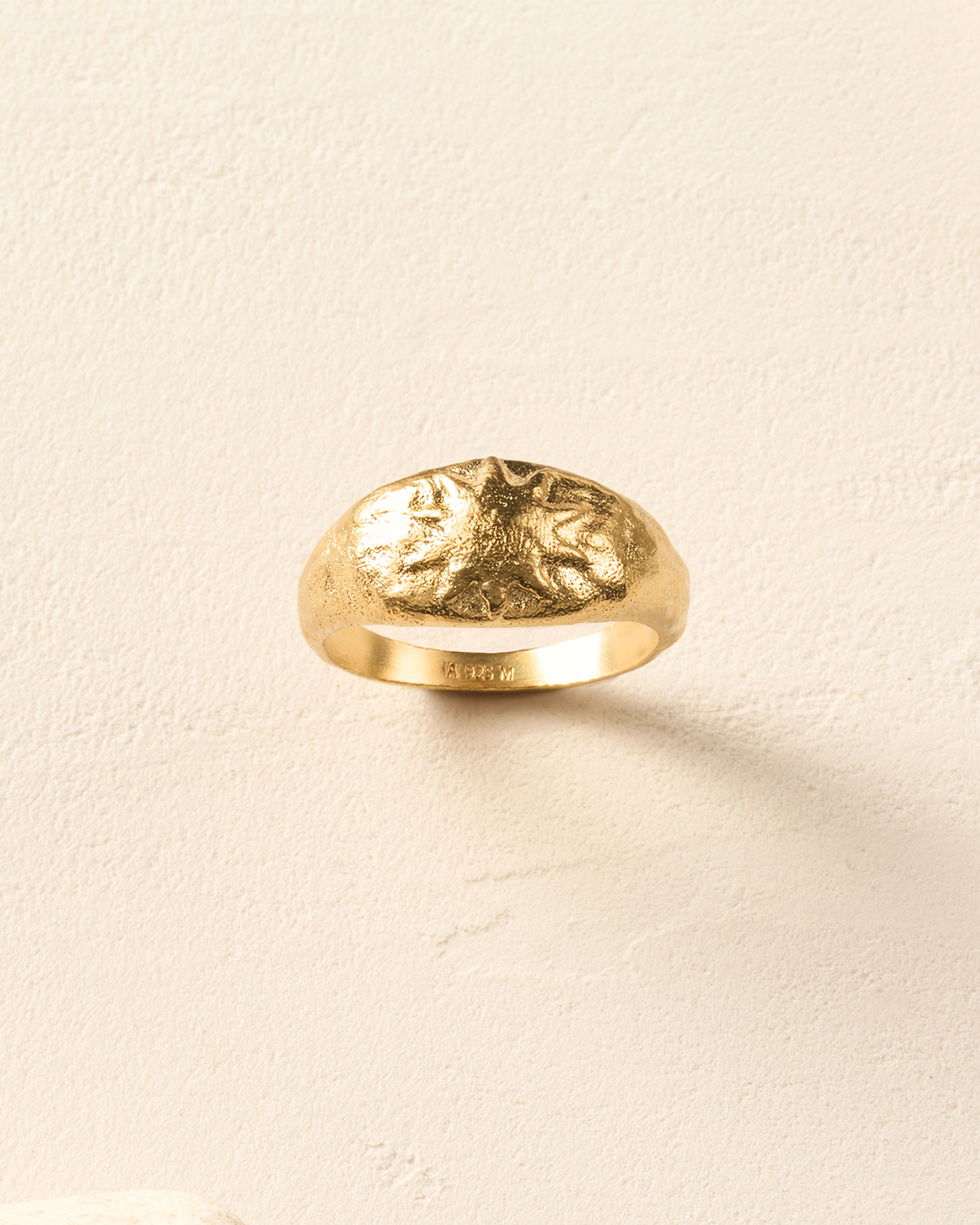 Gold Soléia ring, a hammered dome with an embossed sun design, on a light background.
