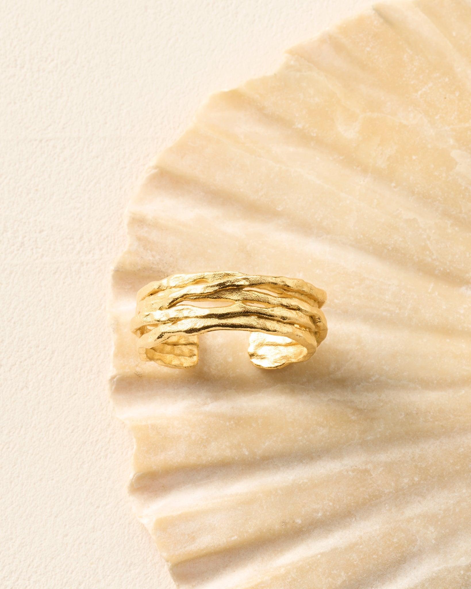 Gold coral ring with organic, textured lines on a light, ribbed seashell.