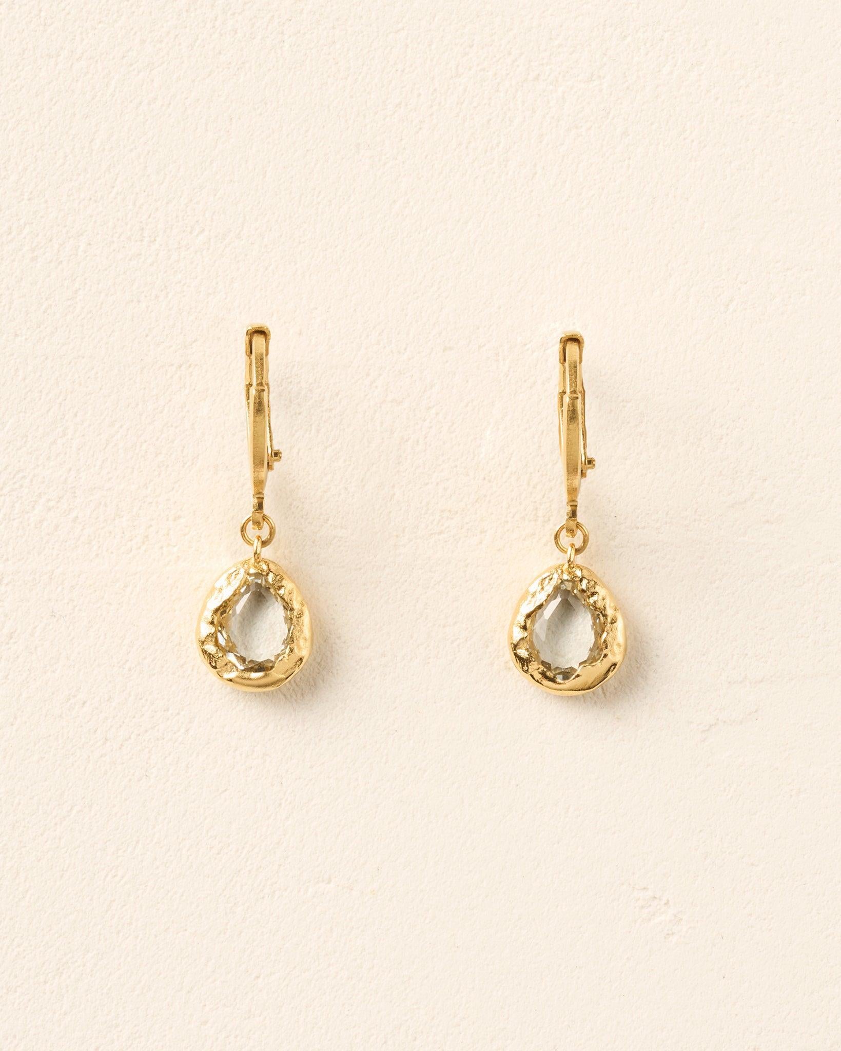 Lysia Crystal Earrings: Gold hoops with drop-shaped pendants, each featuring a white stone in textured gold.