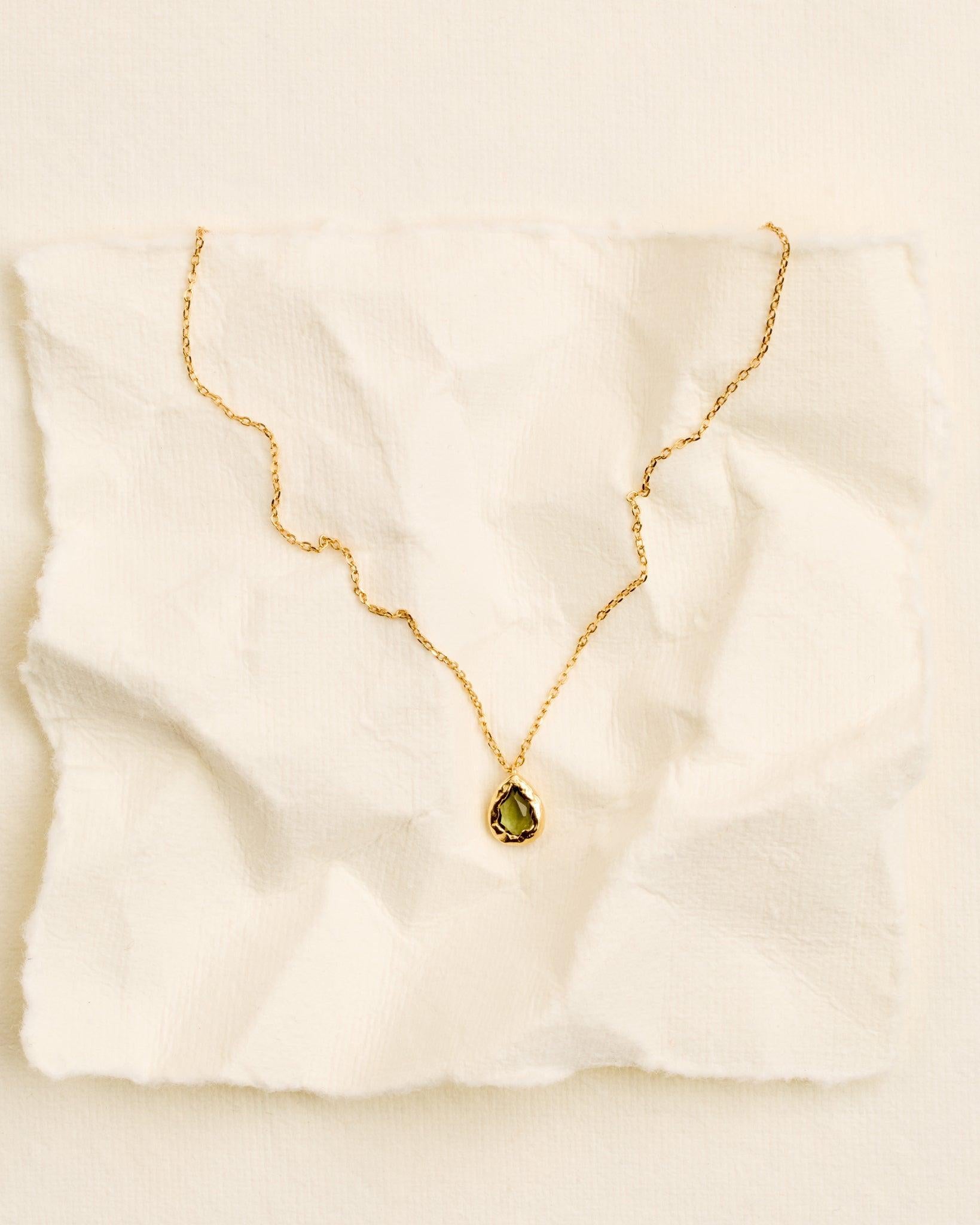 Collier Lysia Mini : chaîne dorée avec un petit pendentif goutte doré texturé, orné d'une pierre vert foncé.