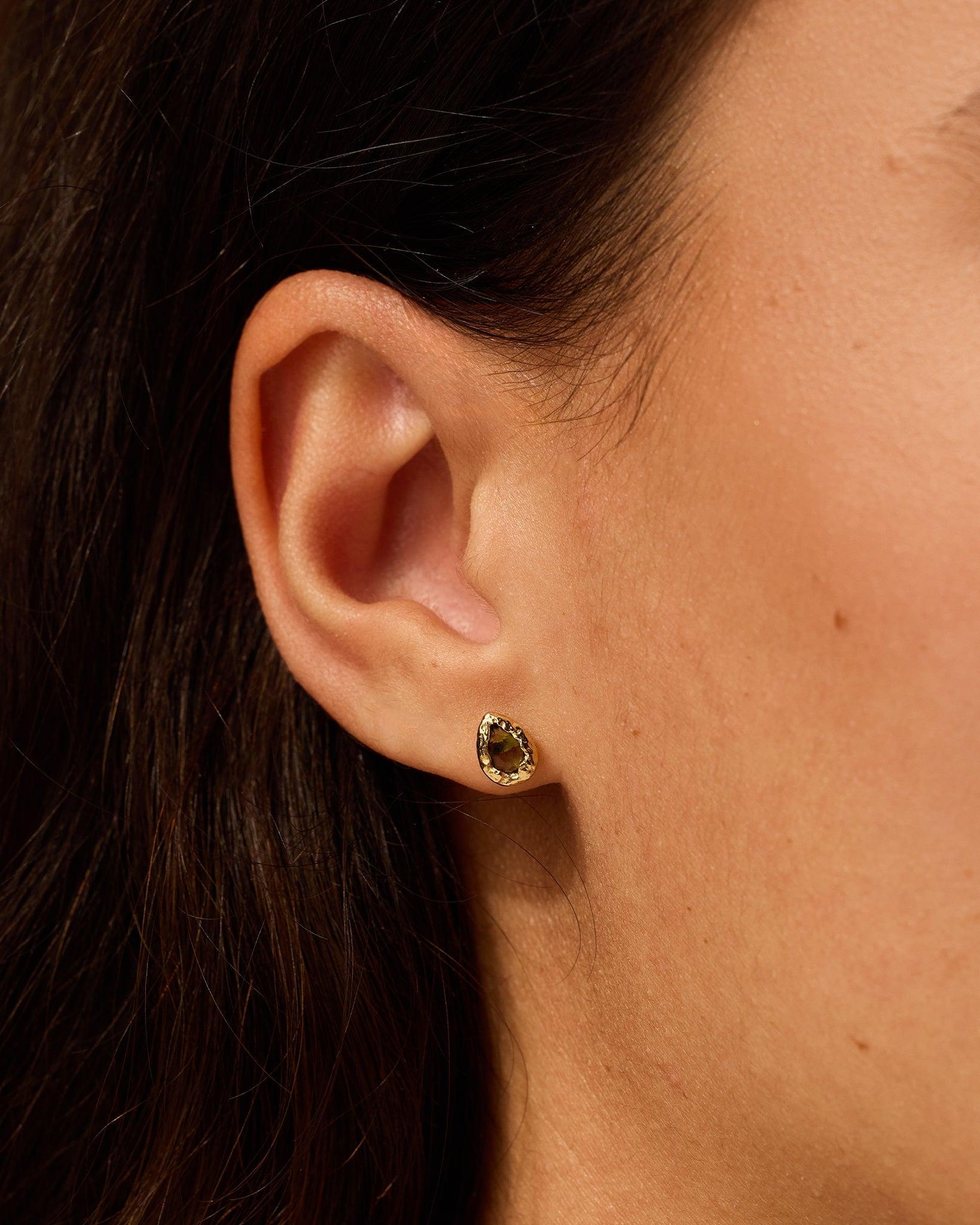 Lysia drop-shaped stud earring with dark-green stone hand-set in textured gold on an ear.