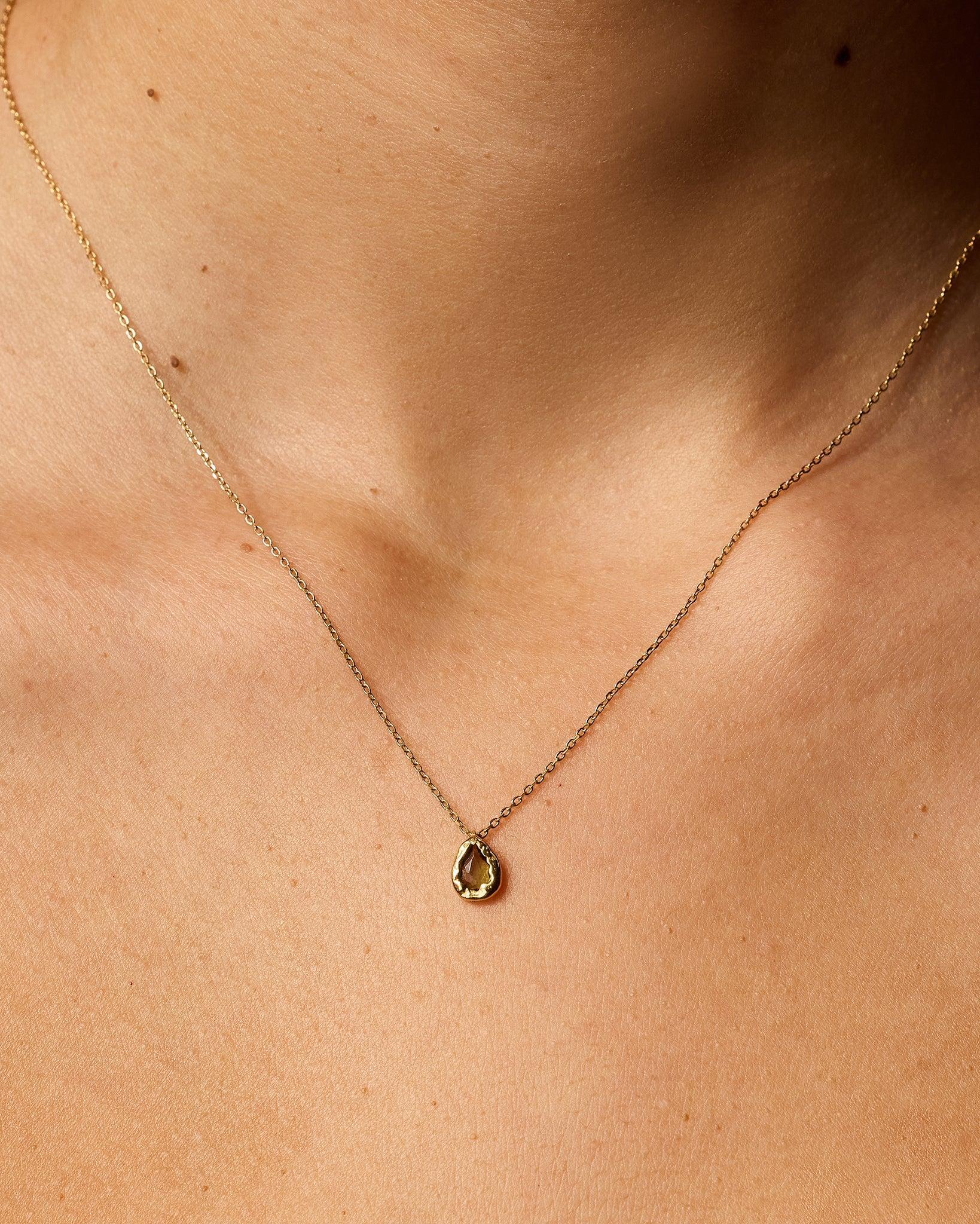Lysia Mini necklace with a small, textured gold, drop-shaped pendant featuring a dark-green stone.