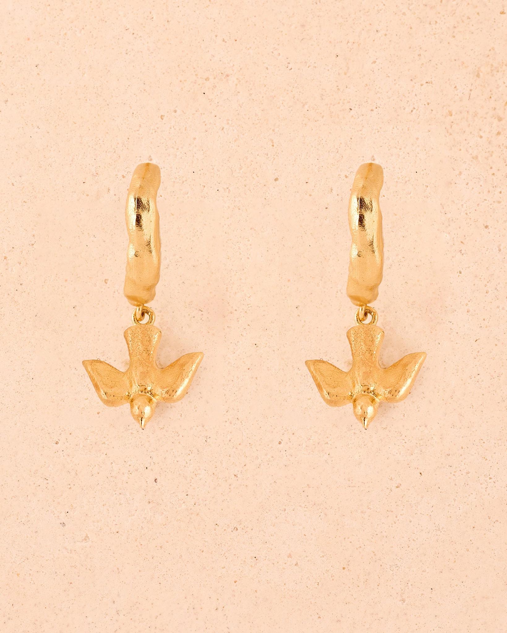 Gold Mara earrings featuring small flying bird pendants suspended from textured mini-hoop earrings.