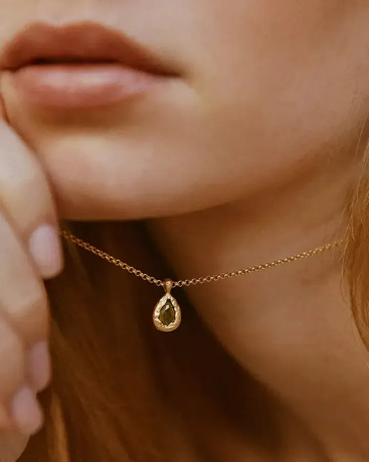 Collier Lysia à pierre vert foncé en forme de goutte, avec pendentif doré texturé, sur une chaîne dorée fine.