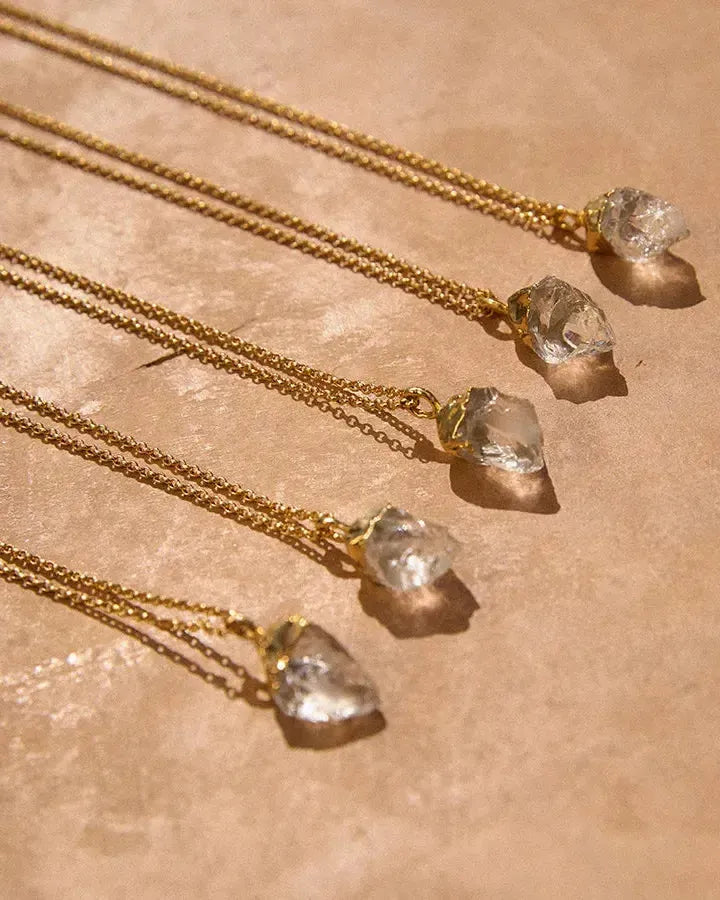 Cinco collares Dioné con colgantes de cuarzo transparente y engastes dorados irregulares, en finas cadenas doradas.