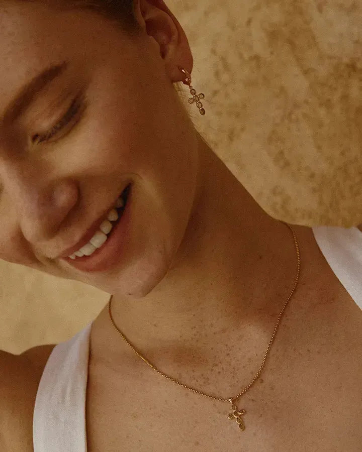 Gold Nexa Necklace with a small cross pendant featuring oval green stones, worn by a smiling woman.