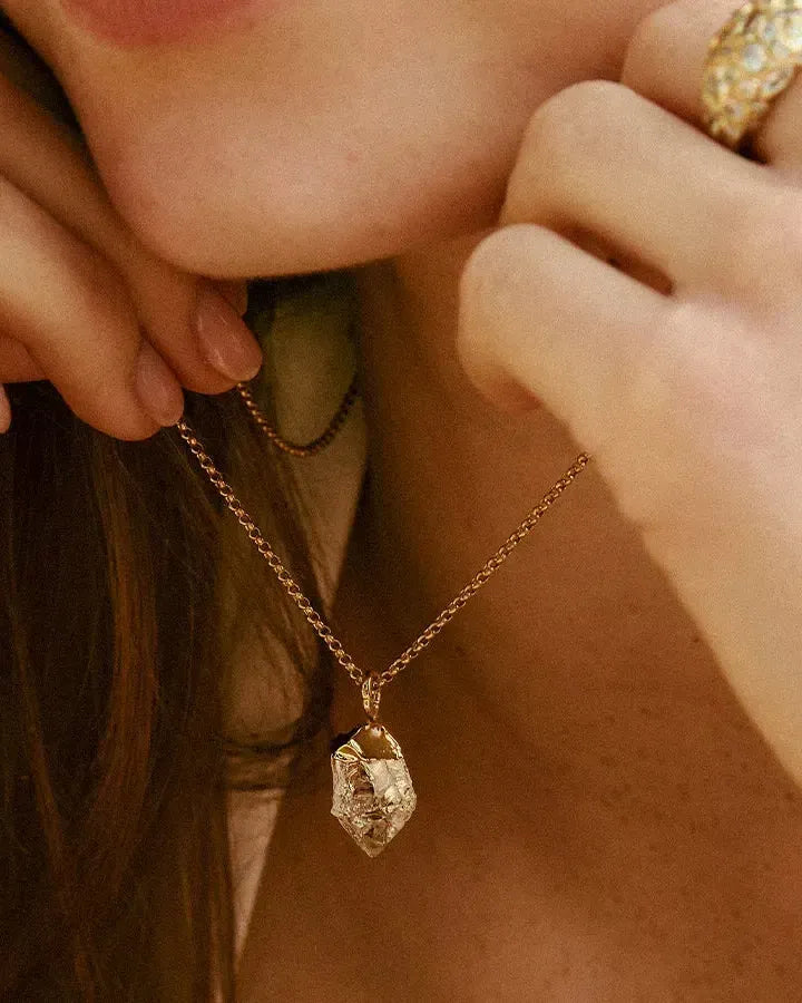 Collar Dioné: colgante de cuarzo transparente con engaste dorado irregular, en una fina cadena dorada, llevado por una persona.