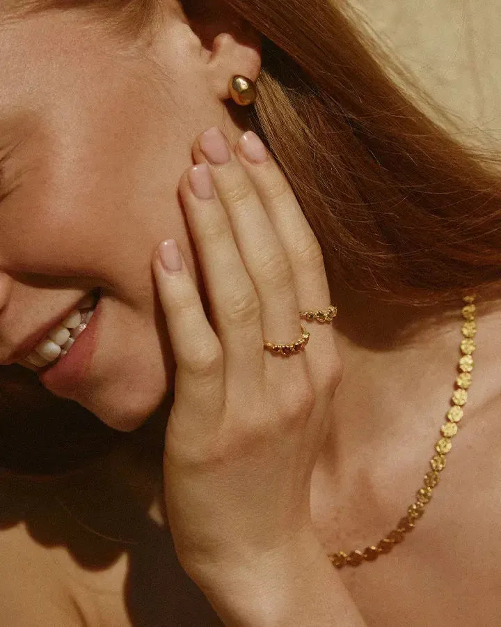 Caius Necklace: Gold chain with small, hammered discs, worn by a smiling woman.
