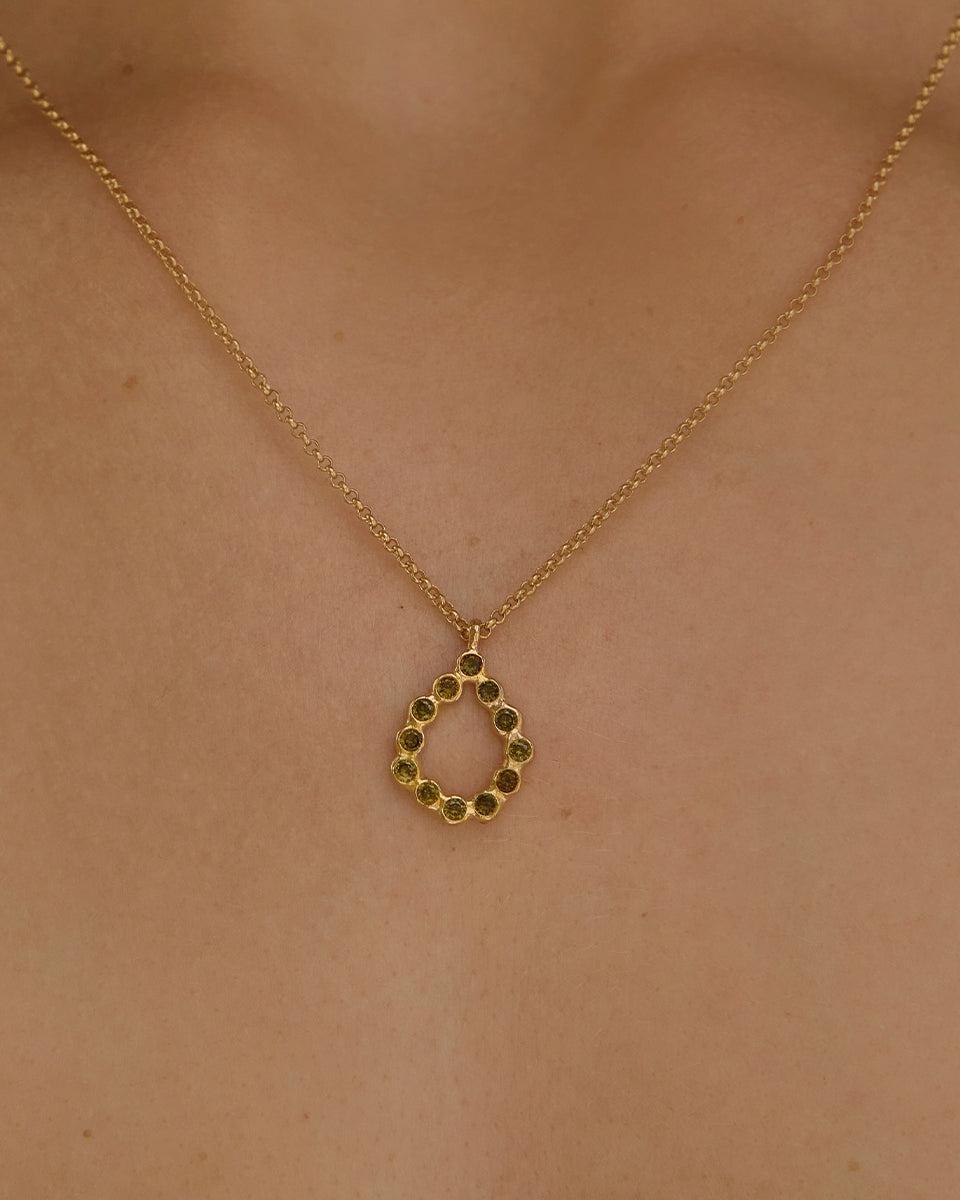 Dunkelgrüne Adelia Halskette mit goldfarbener Kette und geometrischem, tropfenförmigem Anhänger mit grünen Steinperlen.