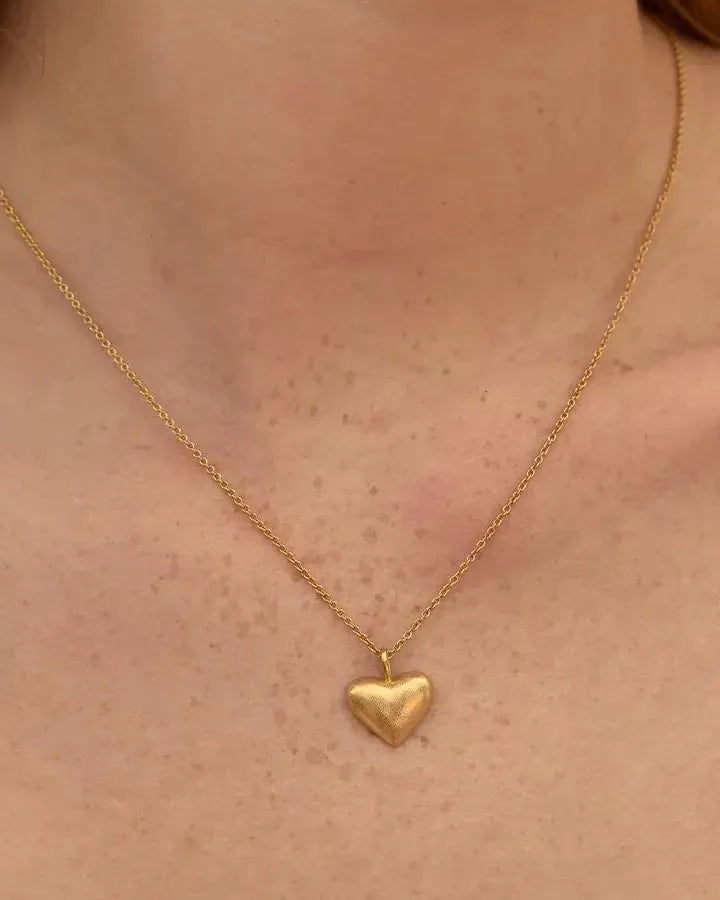 Collar Leona: cadena dorada con colgante de corazón abombado y texturizado, en el pecho.