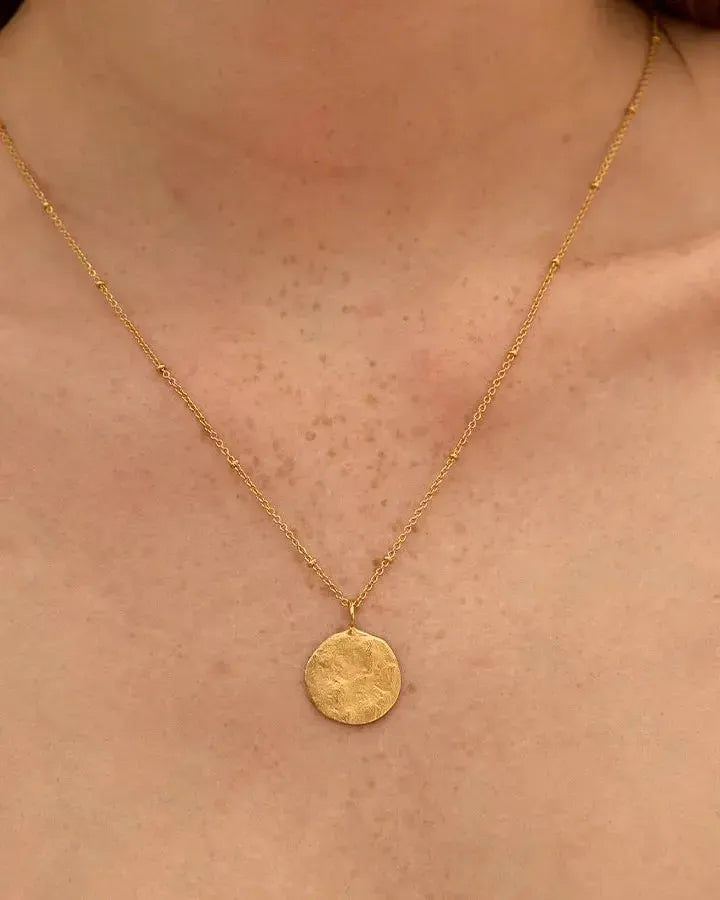 Delicate gold Luna necklace with a hammered full moon pendant on a beaded chain.