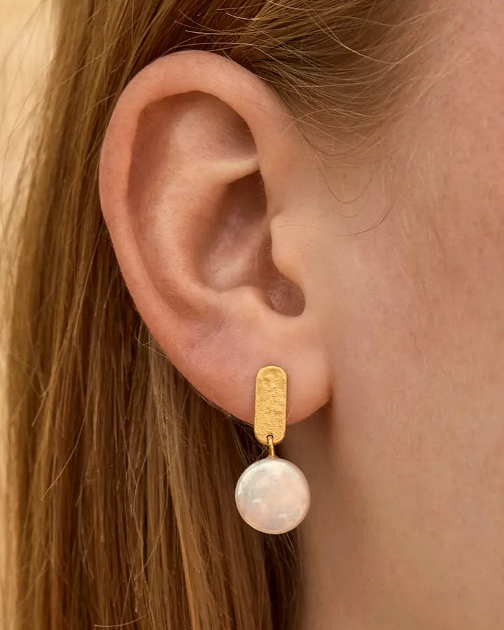 Perla earrings: gold-toned, hammered metal bar with a dangling round white pearl on an ear.