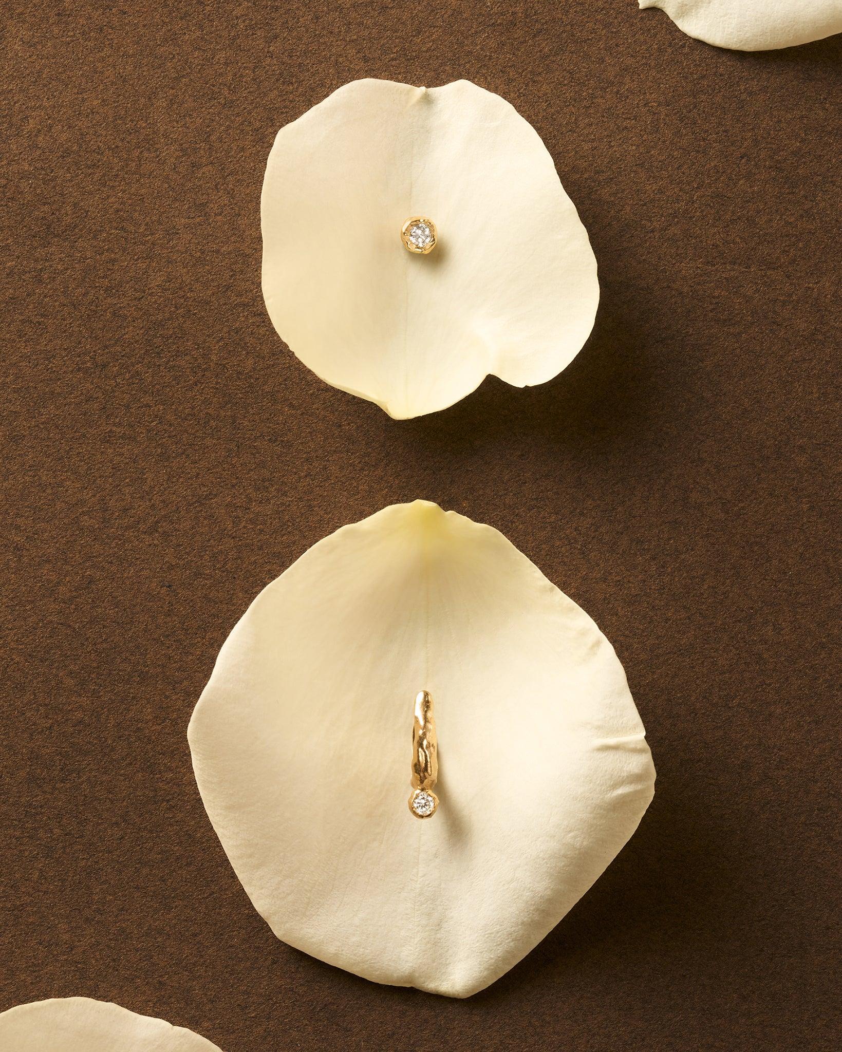 Gold Ada hoop earring with molten texture and a lab-grown diamond on a white rose petal.