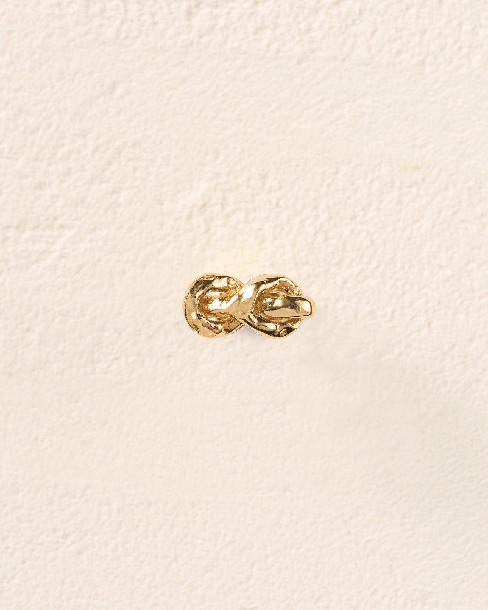 Gold hammered knot piercing stud with two interlocking rope-like strands and a flat-back closure.