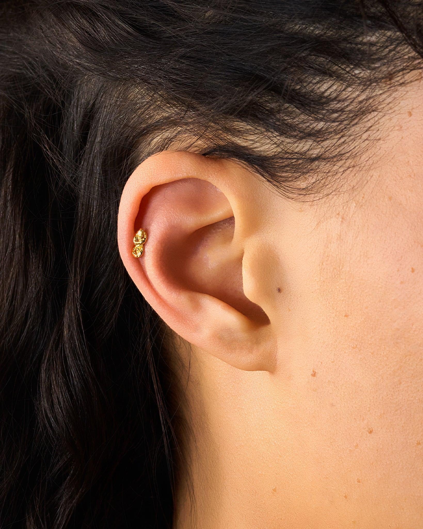 Gold hammered reef knot piercing stud with flat-back closure in a helix piercing.