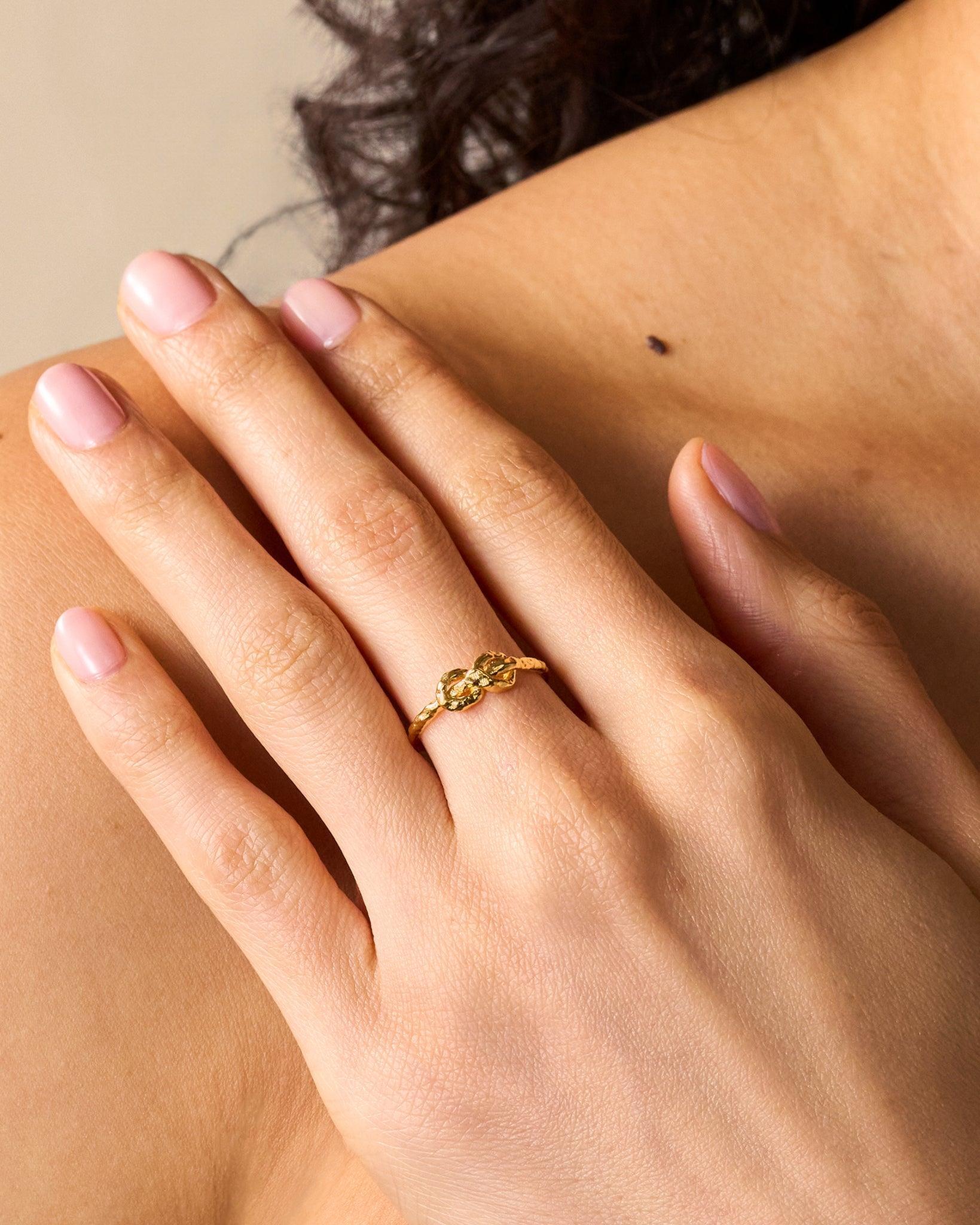 Gold Nodéa Ring: hammered reef knot design with two rope-like strands forming the band, worn on a finger.