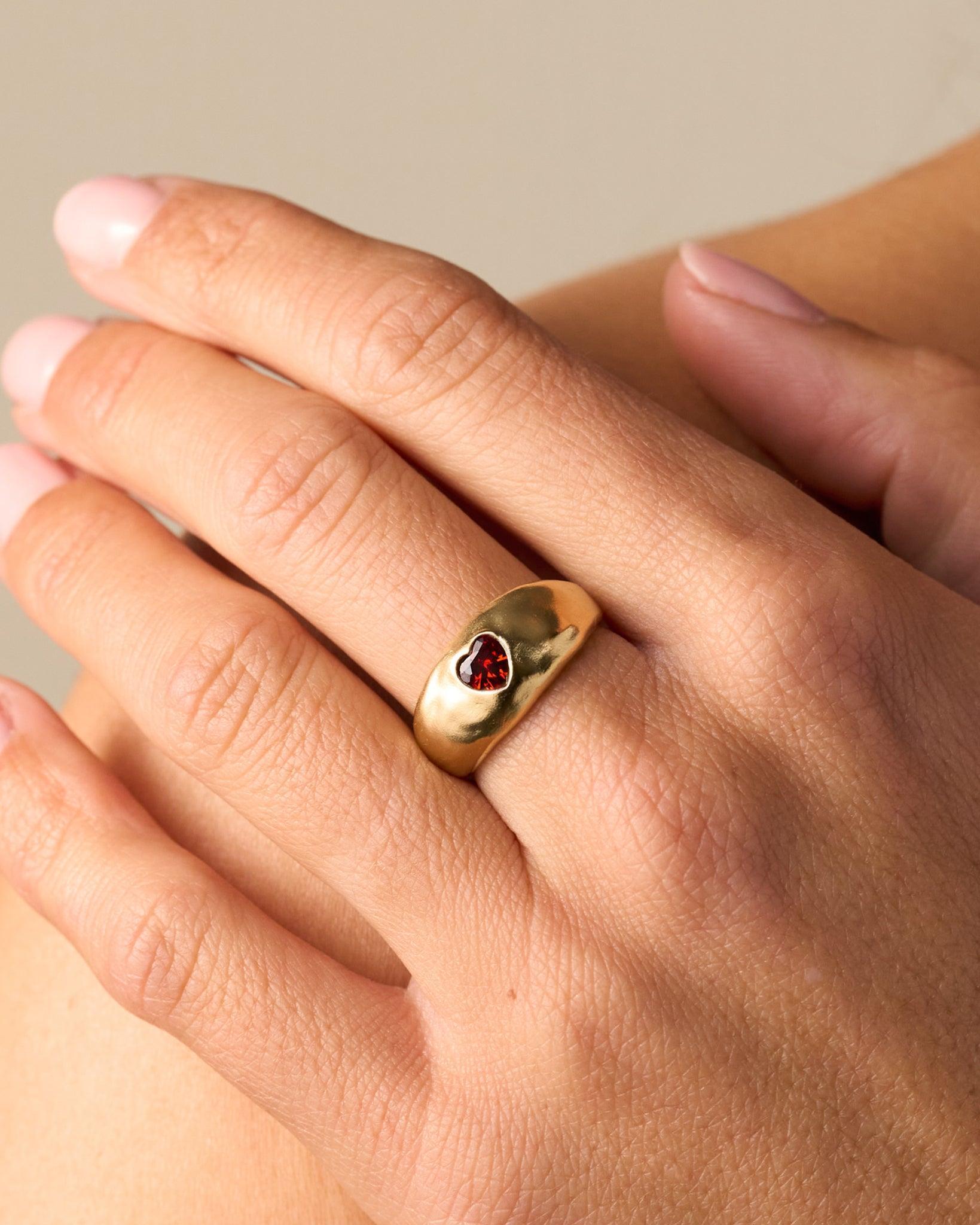 Gold domed ring with a deep red heart-shaped stone on a smooth, slightly hammered surface.