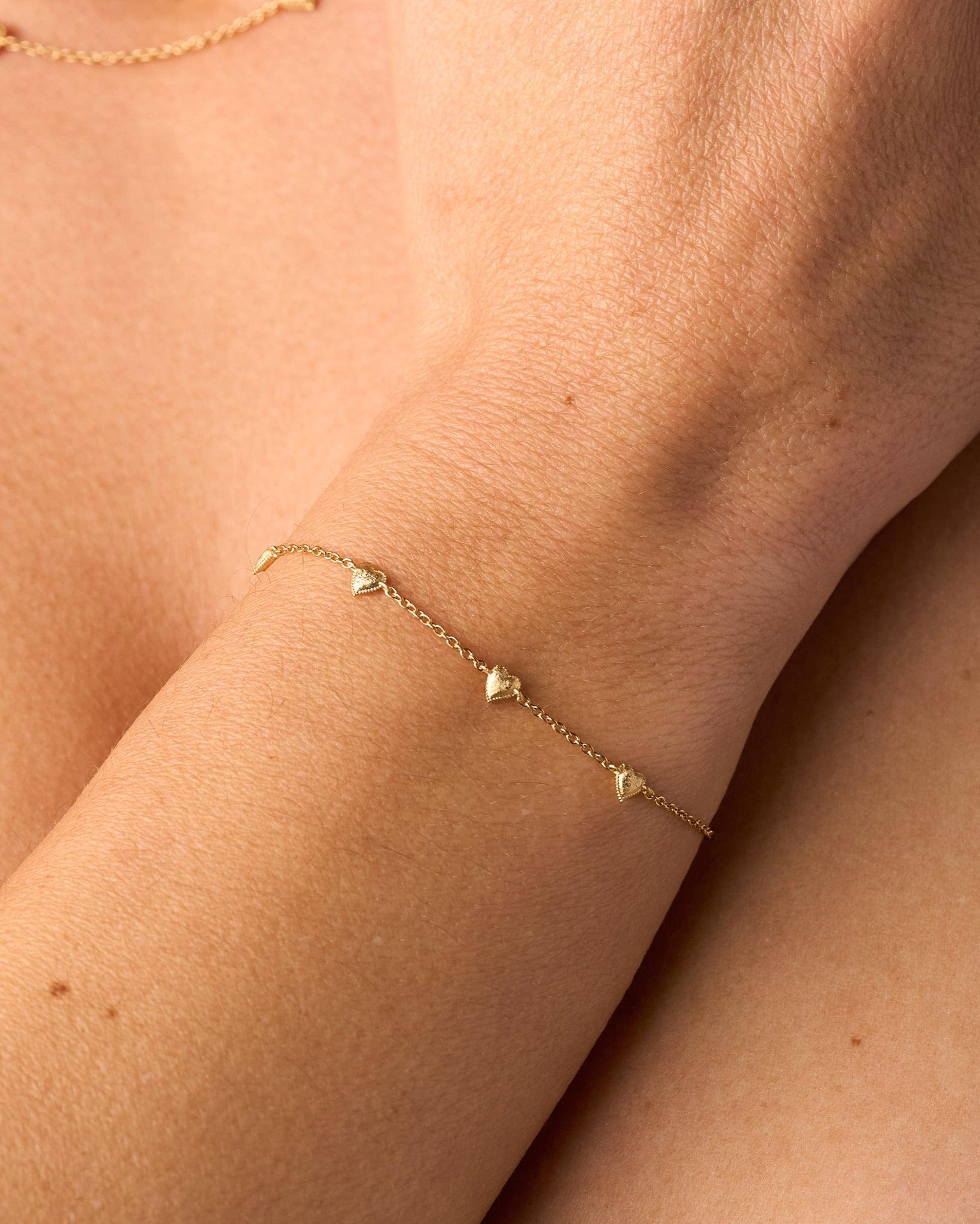 Amori gold bracelet with small, domed, hammered heart charms on a delicate chain.