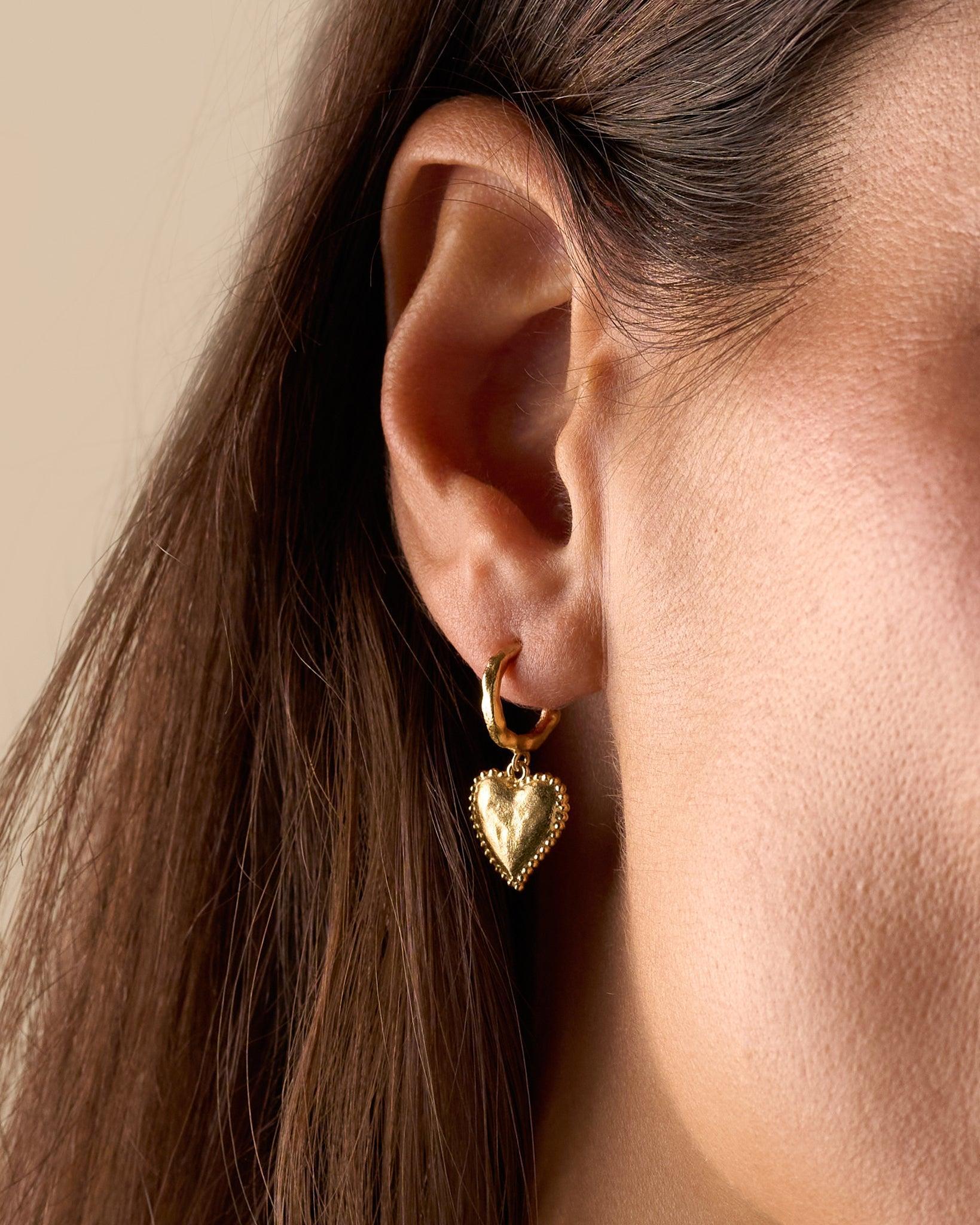 Gold Amori hoop earring with a hammered heart and beaded halo, worn on an ear.