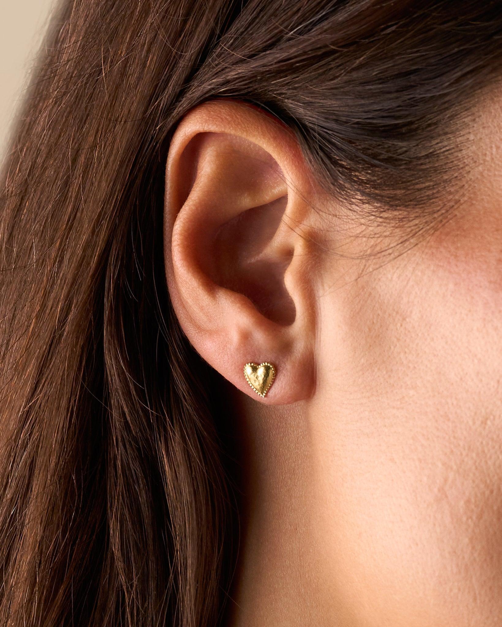 Gold Amori heart stud earring with hammered dome and beaded halo on a woman's ear.