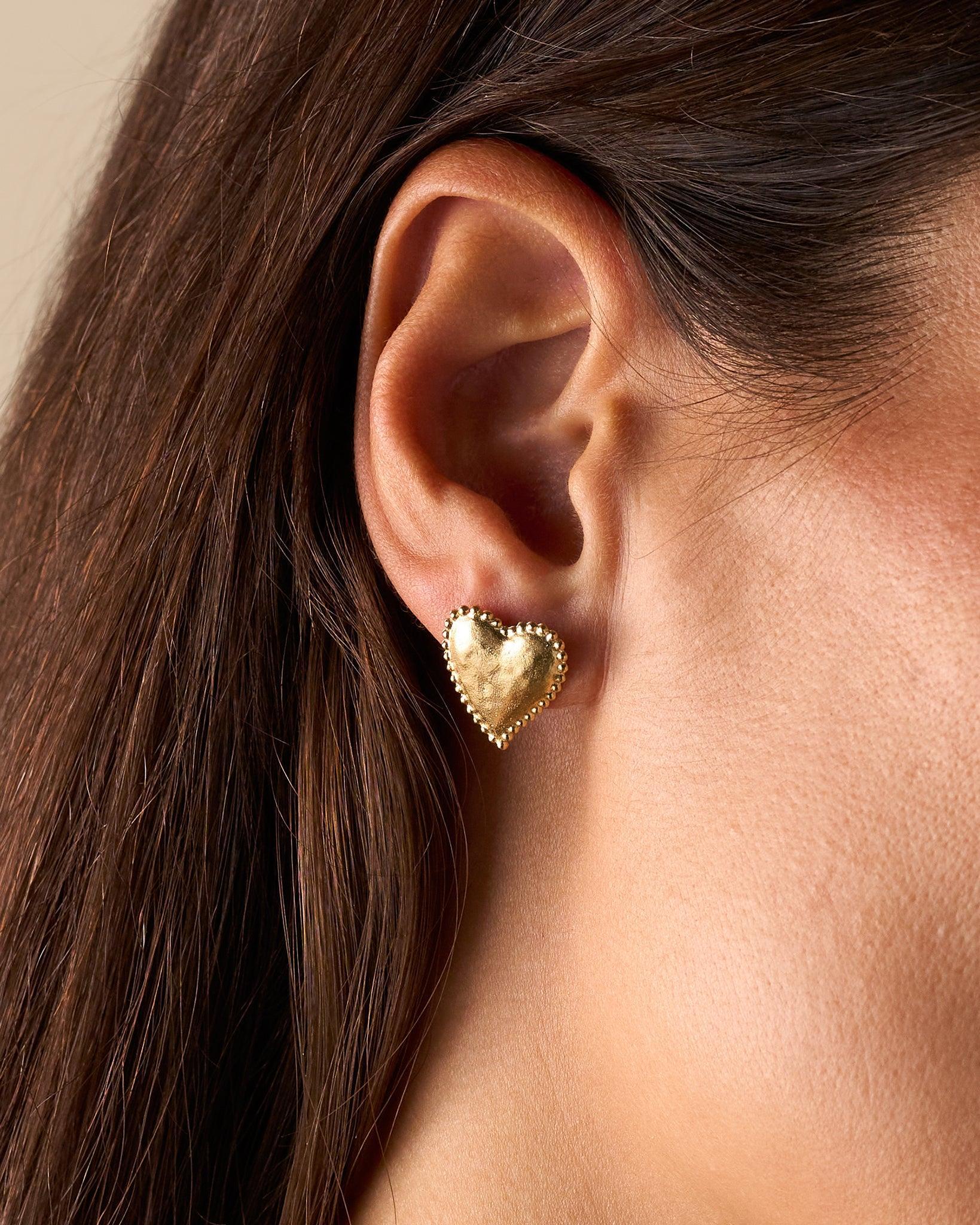 Gold Amori heart earrings with a hammered texture and beaded halo on an ear.