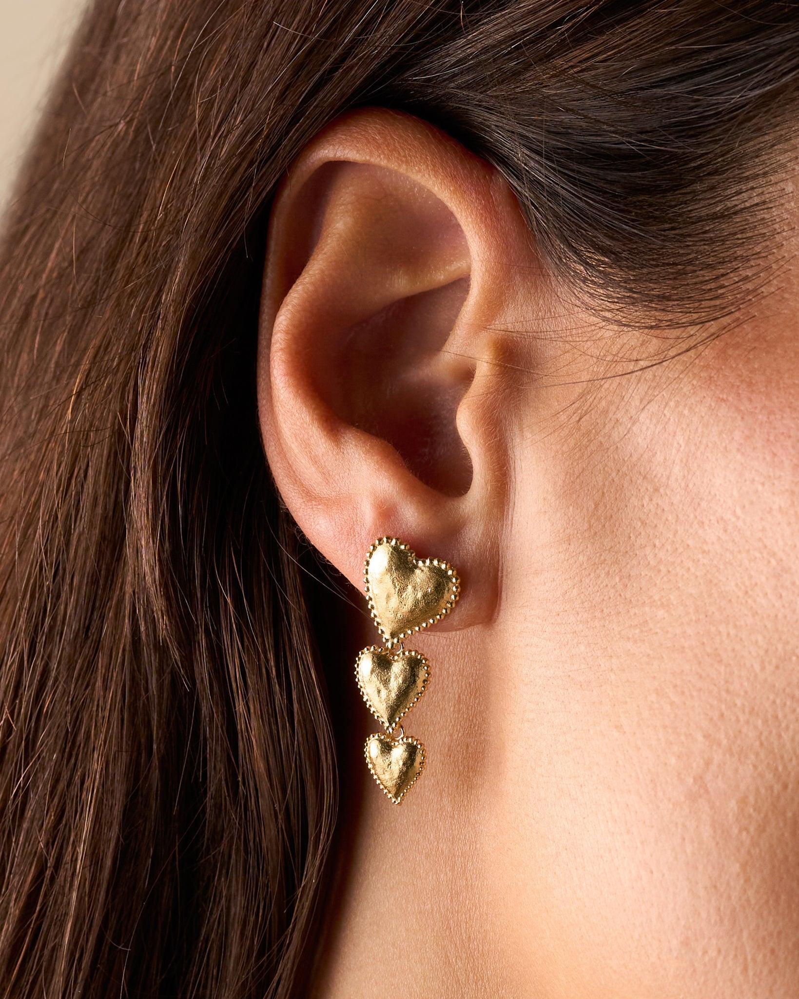 Gold Amori Trio earrings with three stacked, hammered heart drops and beaded halos on an ear.