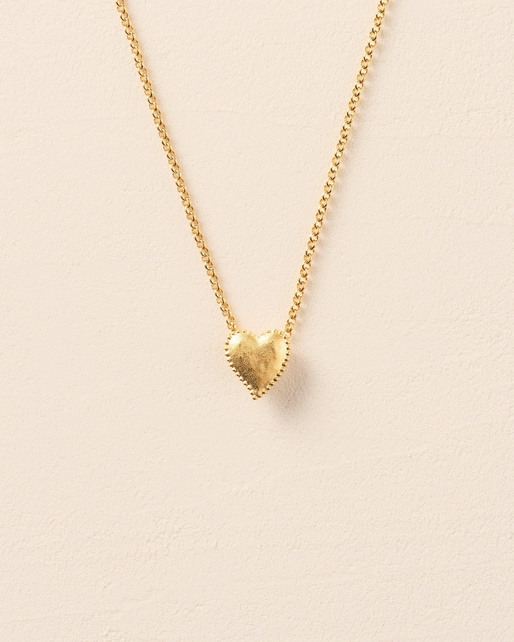Collier Amori doré avec un pendentif cœur martelé et une auréole de perles sur une chaîne fine.