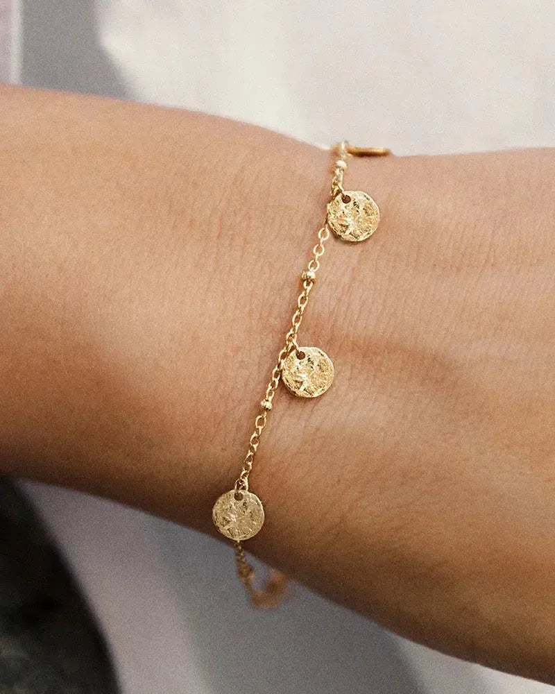 Alceste gold bracelet with a delicate chain and three textured, circular pendants.