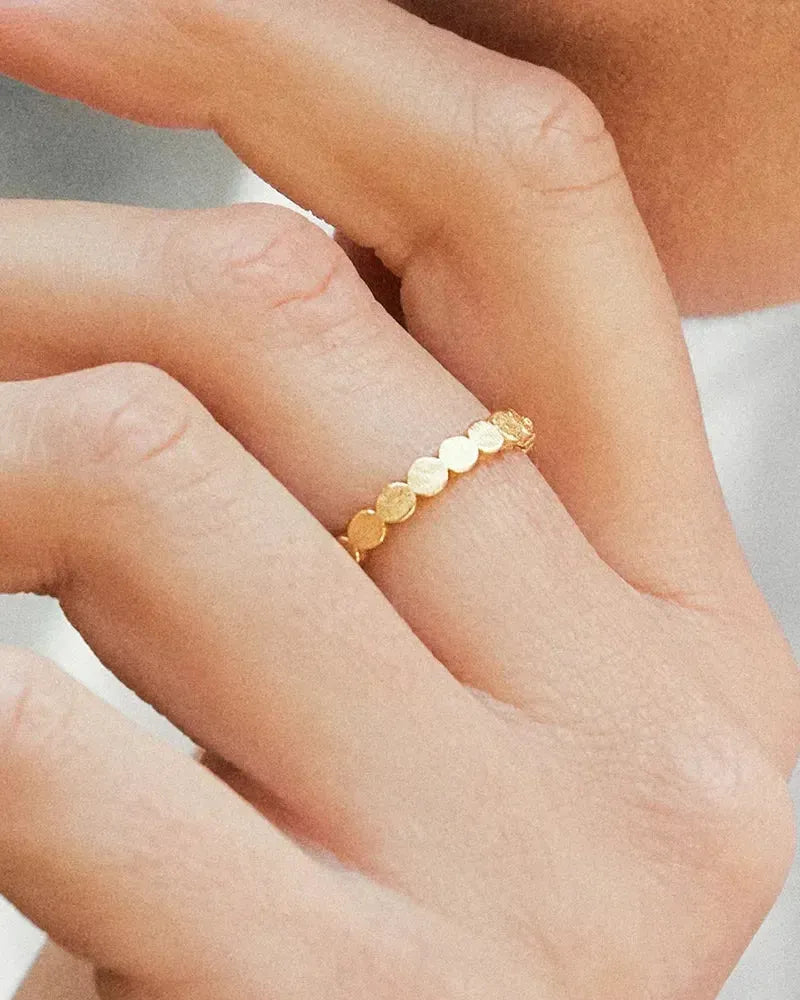 Delicate gold Anatole II ring with a band of small, flat, circular discs on a finger.