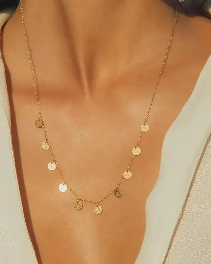 Alceste gold necklace with ten delicate, hammered circular pendants on a thin chain, worn on a woman's neck.