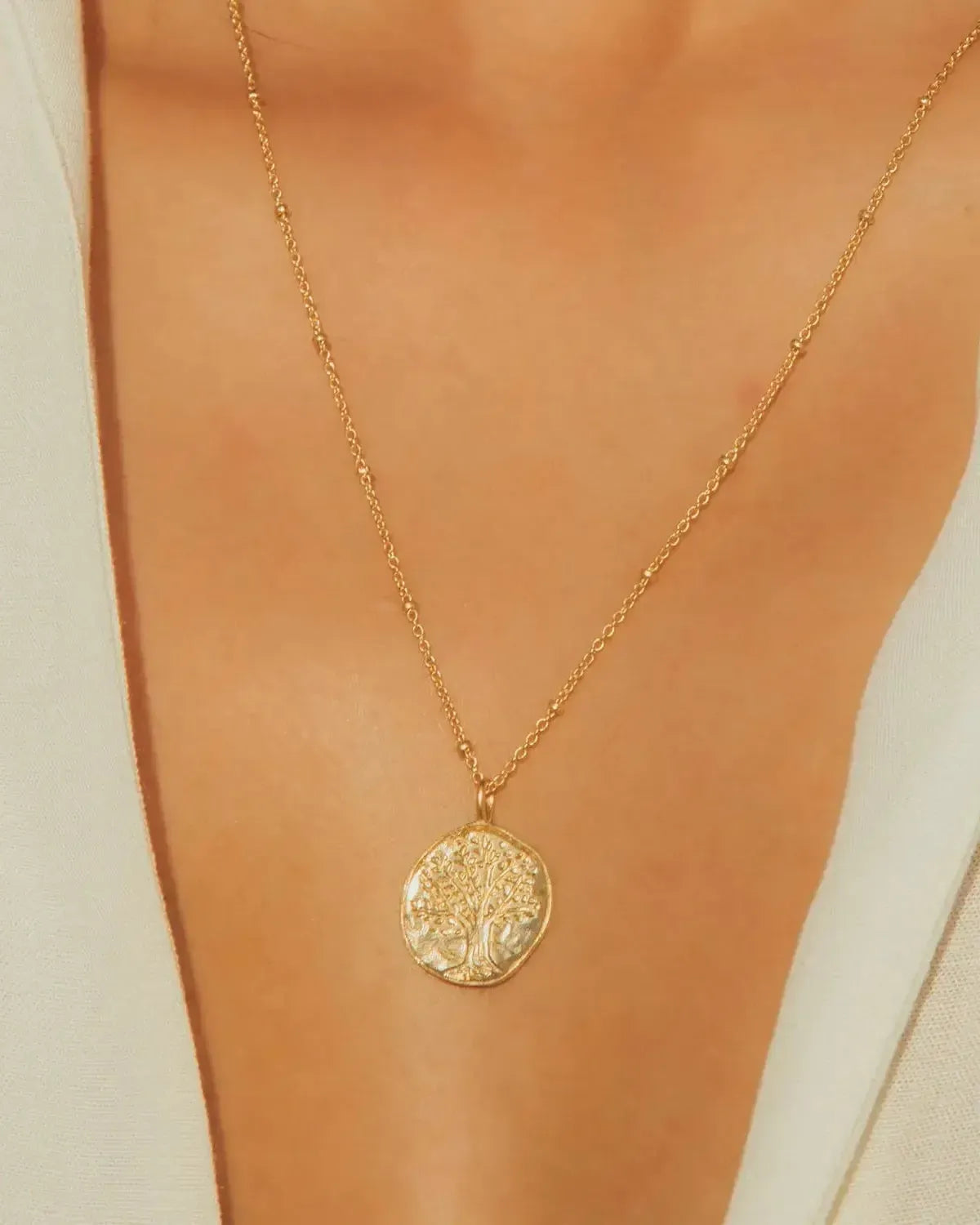 Gaya gold Tree of Life necklace with a round, textured pendant on a delicate beaded chain.