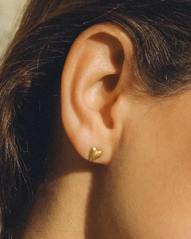 Close-up of a single small, textured gold heart stud earring on an ear.