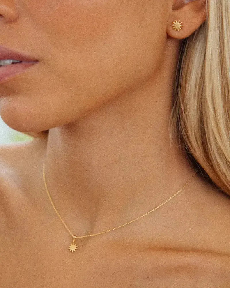 Pendientes de botón de sol dorados y collar con colgante de sol a juego, en una mujer.
