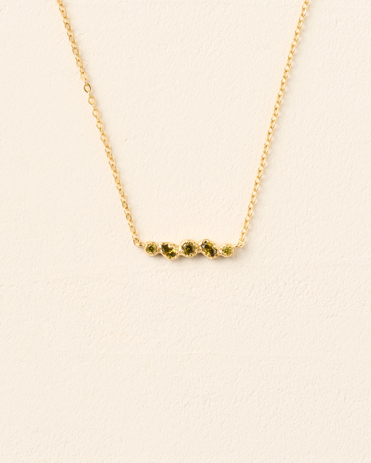 Collar de cadena dorado con un colgante horizontal con cinco piedras orgánicas verde intenso en un engaste texturizado.