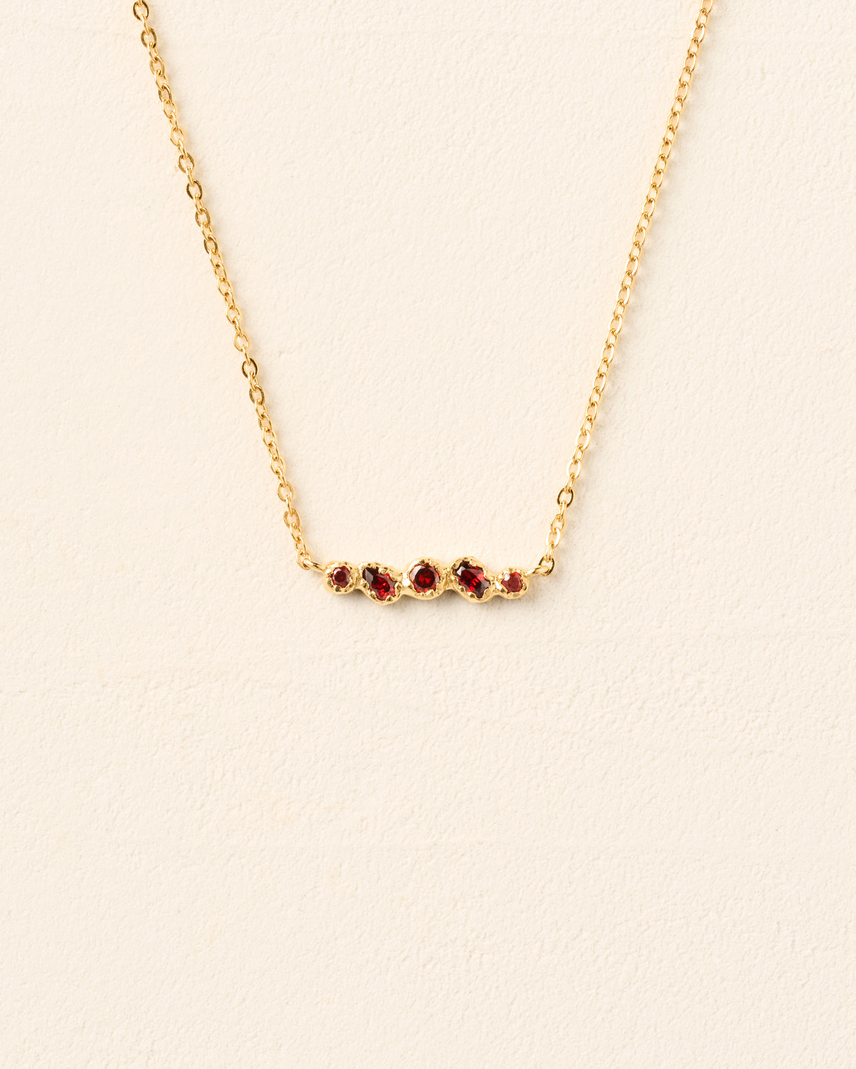 Collar de cadena dorado con un delicado colgante con cinco piedras rojo intenso engastadas a mano en un engaste orgánico e irregular.