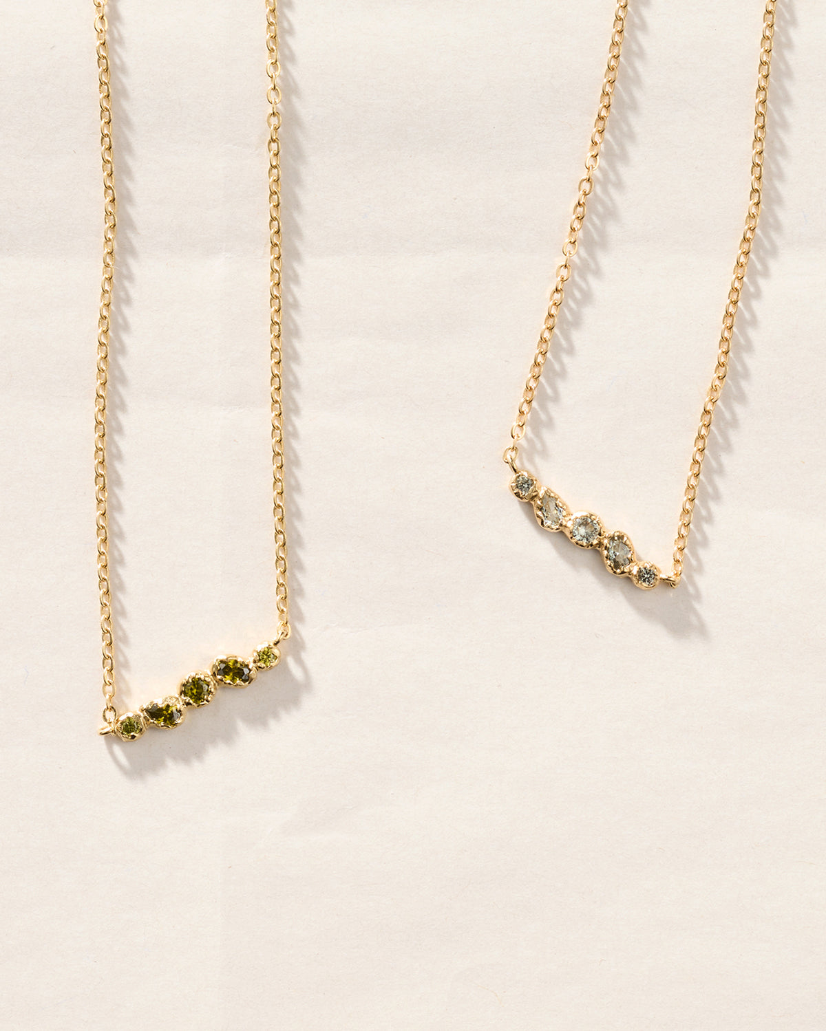 Deux colliers chaîne dorés à pendentifs ornés de cinq pierres céladon bleu-vert aux formes organiques, en une rangée délicate et irrégulière.