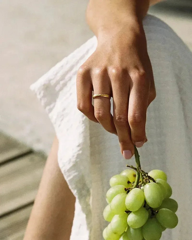 Hand wearing a minimalist gold Bellina ring with a single twist, holding a bunch of green grapes.