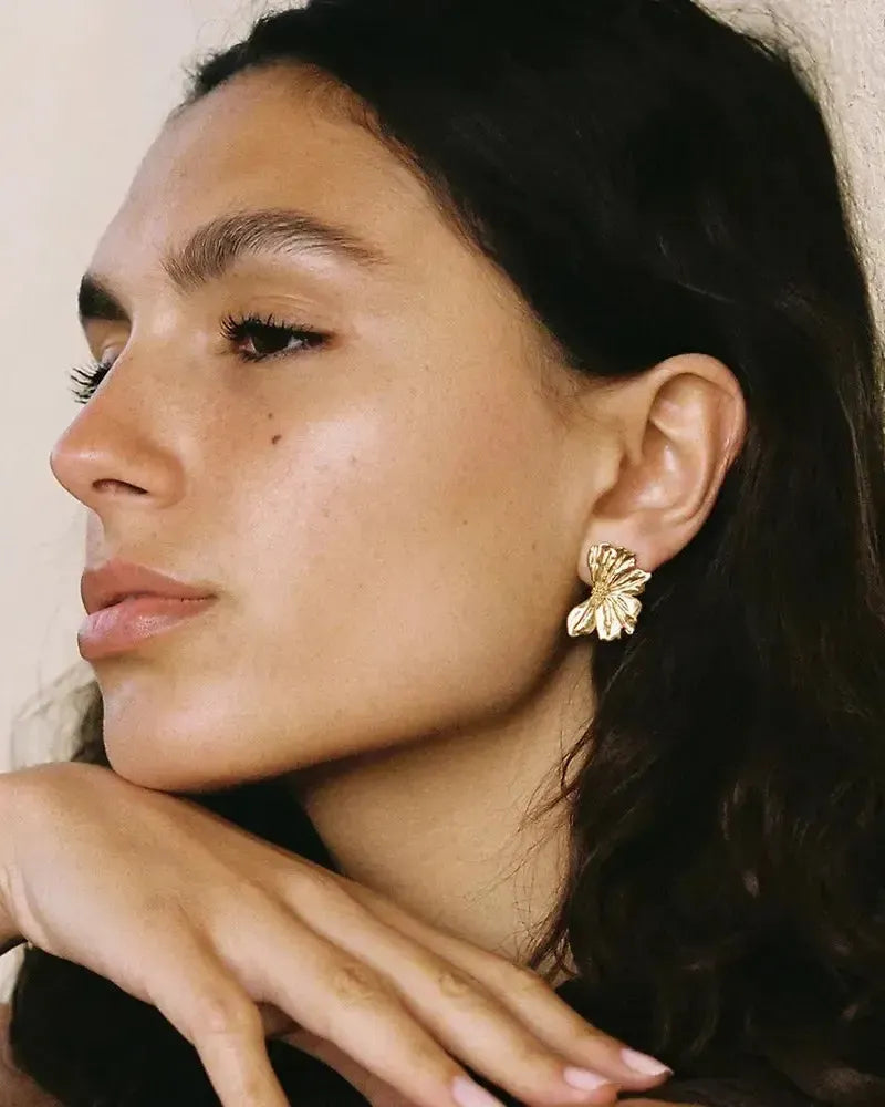 Pendientes de media flor Monea dorados en la oreja de una mujer, mostrando su diseño delicado y texturizado.