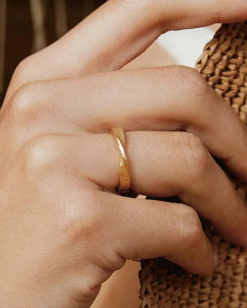 Bellina gold twisted band ring on a finger, featuring a minimalist modern design.