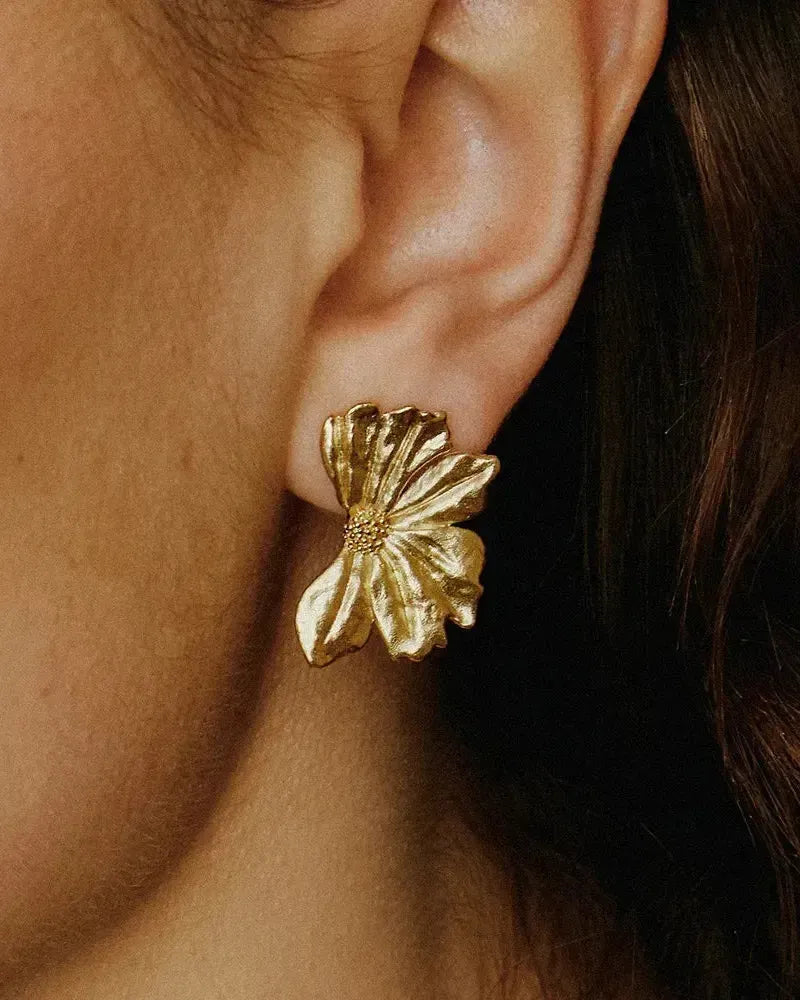 Gold-toned Monea half-flower earrings with textured petals and a delicate center, worn on an ear.