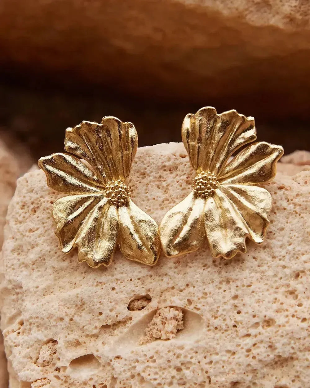Pendientes de media flor Monea: motivo de anémona dorado texturizado con pétalos delicados y centro de cuentas, apoyados sobre una piedra de color claro.