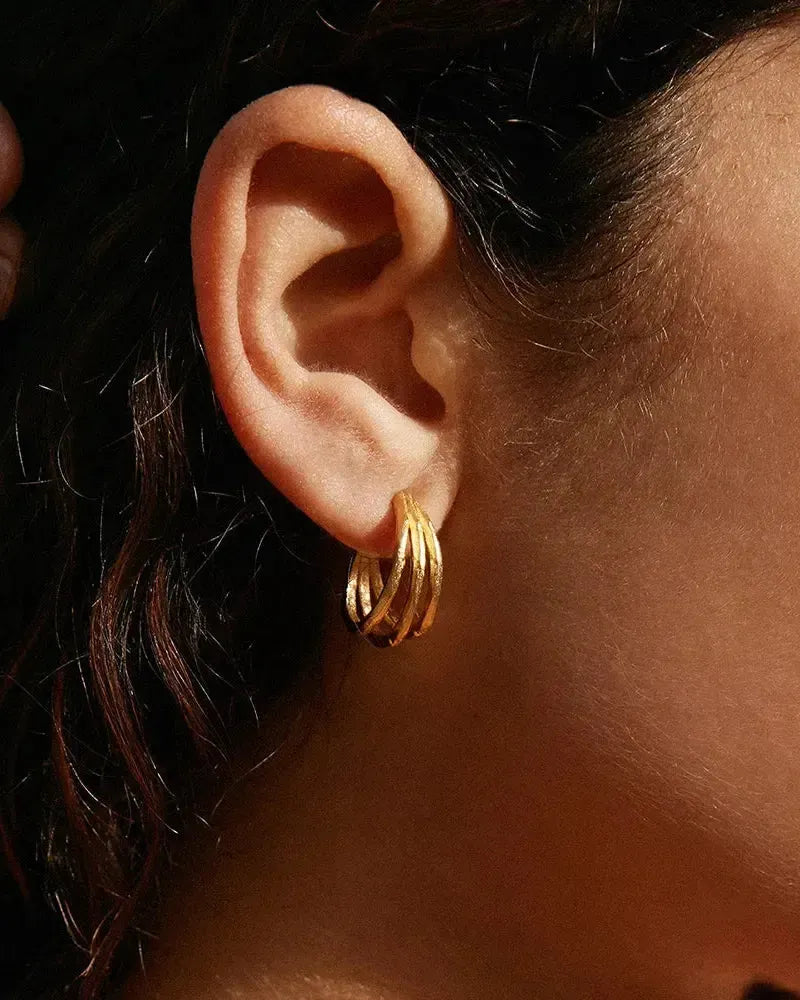 Gold Zéphir Trio hoop earrings with irregular hammered patterns on a model's ear.