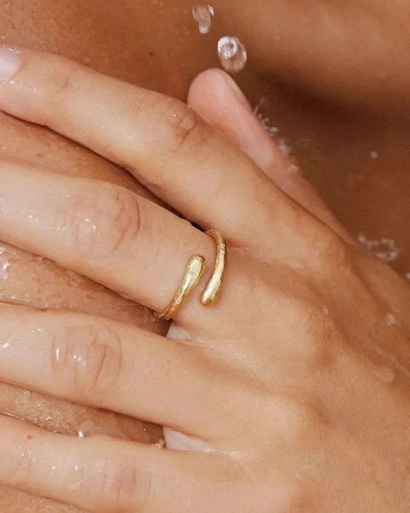 Gold Filippa Mini Ring with bended arc and crossover curves on a wet finger.