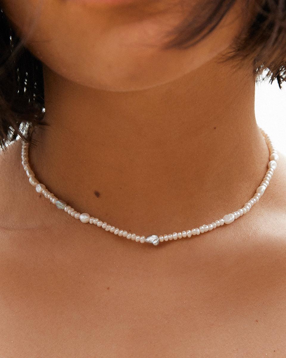 Ras-de-cou Oia : collier de perles fait main avec des perles d'eau douce blanches et grises, au cou d'une femme.