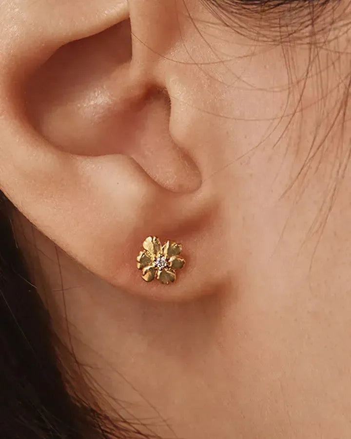 Gold Aleli floral stud earring with a luminous white stone, worn on an ear.