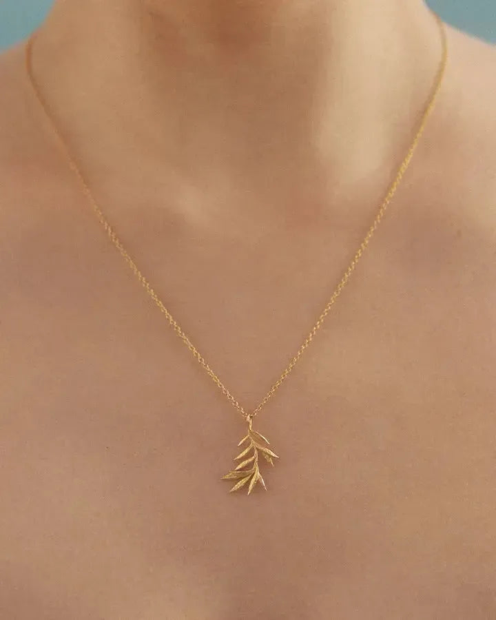 Delicate gold olive branch pendant necklace on a slim chain, worn on a person's chest.